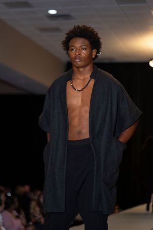 Model showcases dark oversized cardigan with open chest on fashion runway.