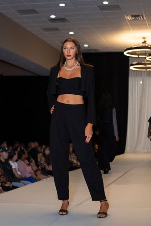 Model showcases sleek all-black ensemble with crop top and wide-leg pants on fashion runway.