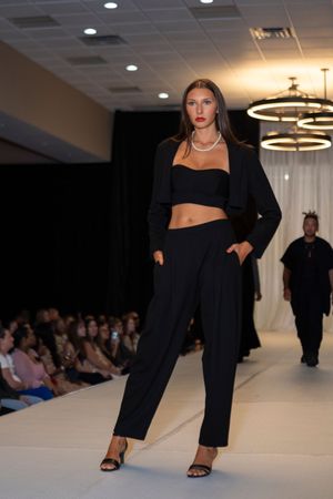 Model showcases black crop top and wide-leg pants ensemble with blazer on runway.