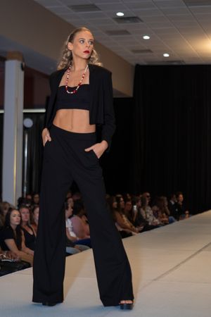 Model walks runway in black crop top and wide-leg trousers with statement necklace.