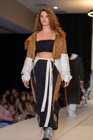 Model showcases casual streetwear look with brown jacket and white sleeves on catwalk.
