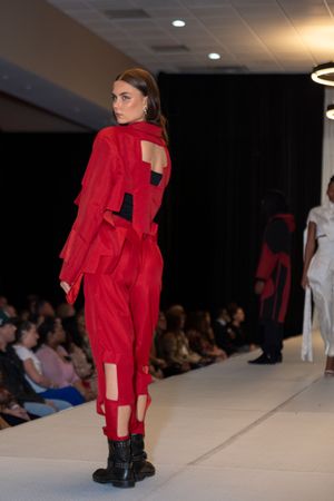 Model showcases dramatic red ruffled dress with combat boots on white runway during fashion show.