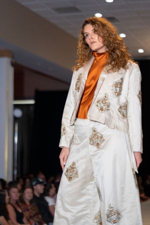 White embellished suit paired with orange turtleneck displayed on fashion runway.