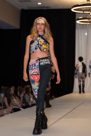 Model showcases edgy streetwear with graphic prints and combat boots on catwalk.