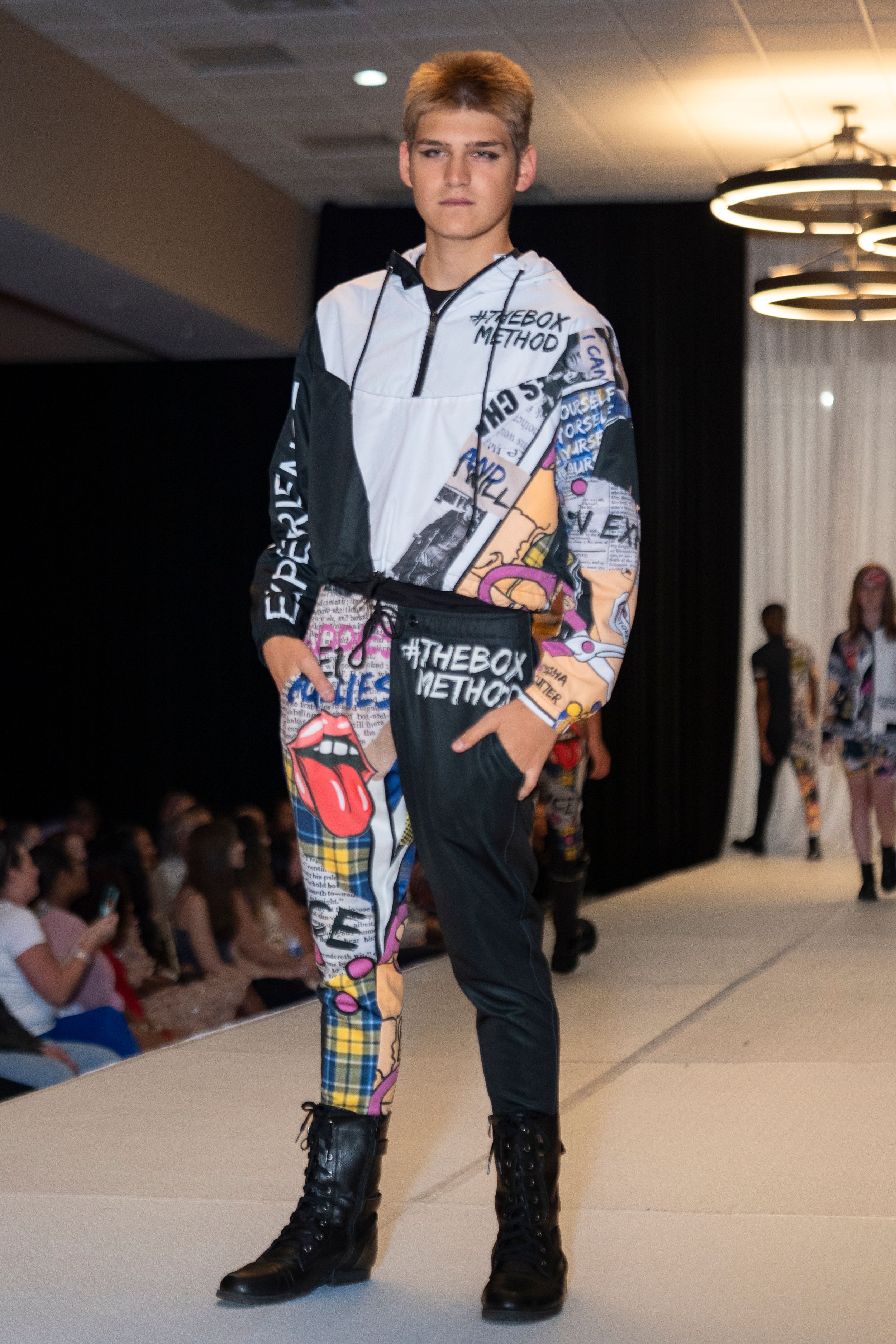 Streetwear look featuring graphic print hoodie and patterned pants with combat boots on catwalk.