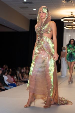 Iridescent holographic dress shimmers under runway lights at fashion show.