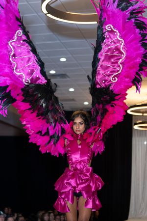 Performer wearing vibrant pink feathered costume with black accents on fashion runway.