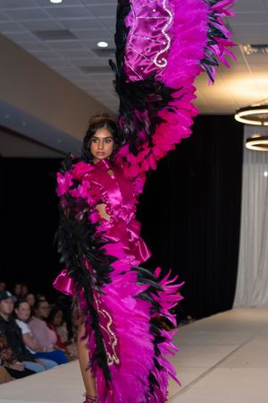 Fashion model wearing dramatic hot pink and black feathered costume walks runway at fashion show.