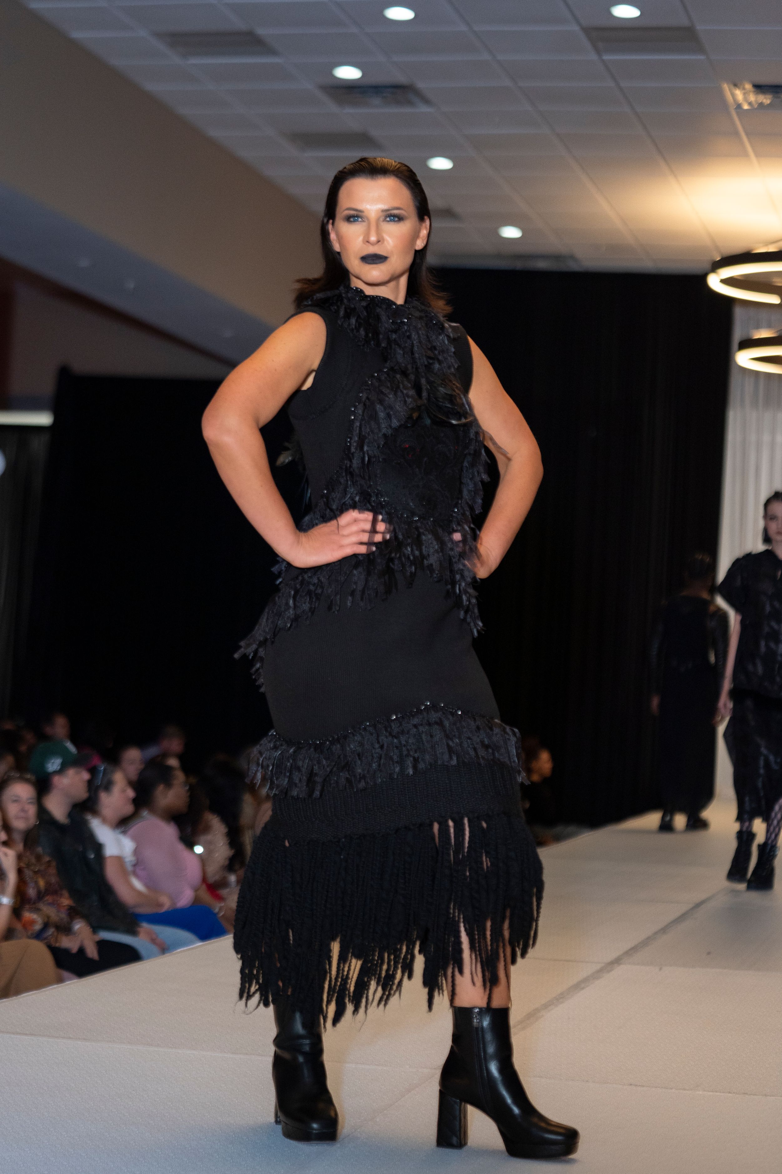 Black fringe dress with matching boots displayed on fashion runway.