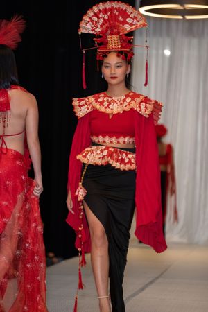 Traditional Asian-inspired red ensemble with ornate headdress and split skirt on fashion runway.