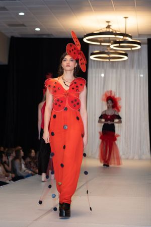 Red ladybug-inspired costume with polka dots displayed during fashion show performance.