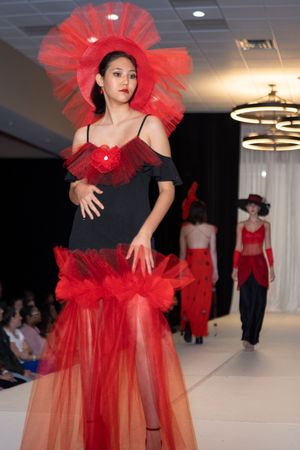 Dramatic red tulle gown with black bodice presented at indoor fashion show.