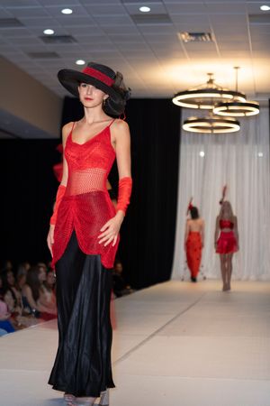 Red lace top paired with black skirt and vintage hat shown on fashion catwalk.