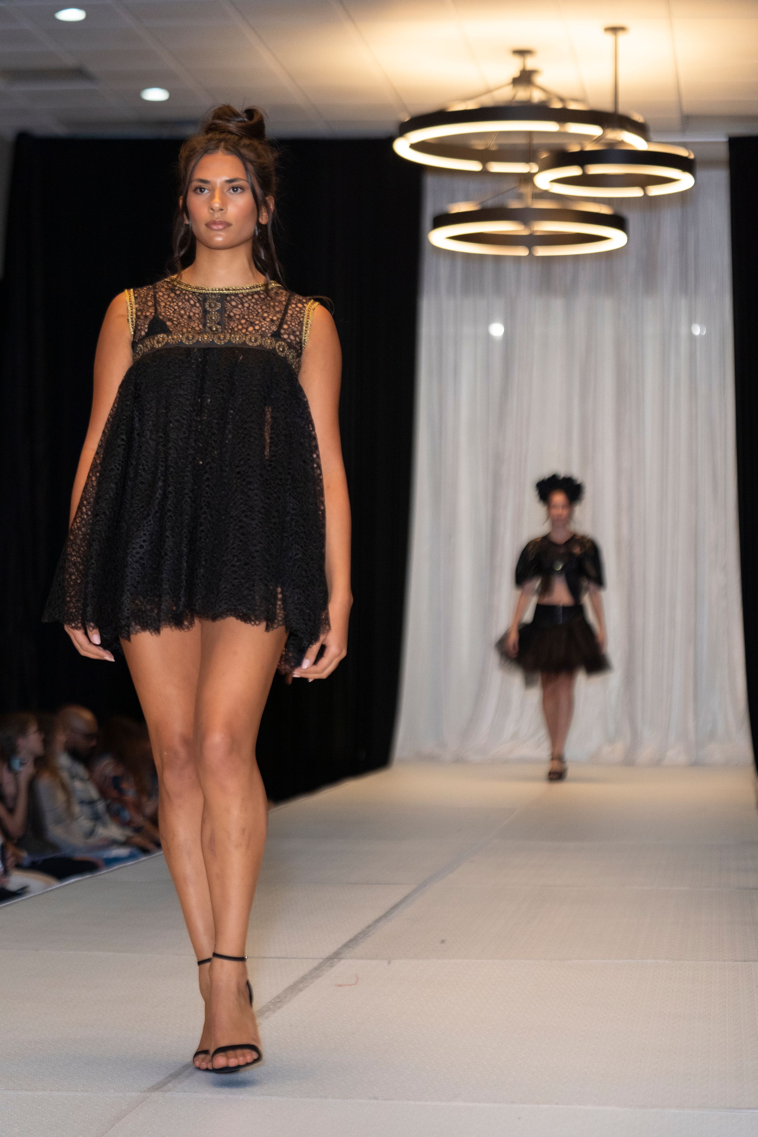 Little black dress with lace detail and flowing silhouette showcased on catwalk.