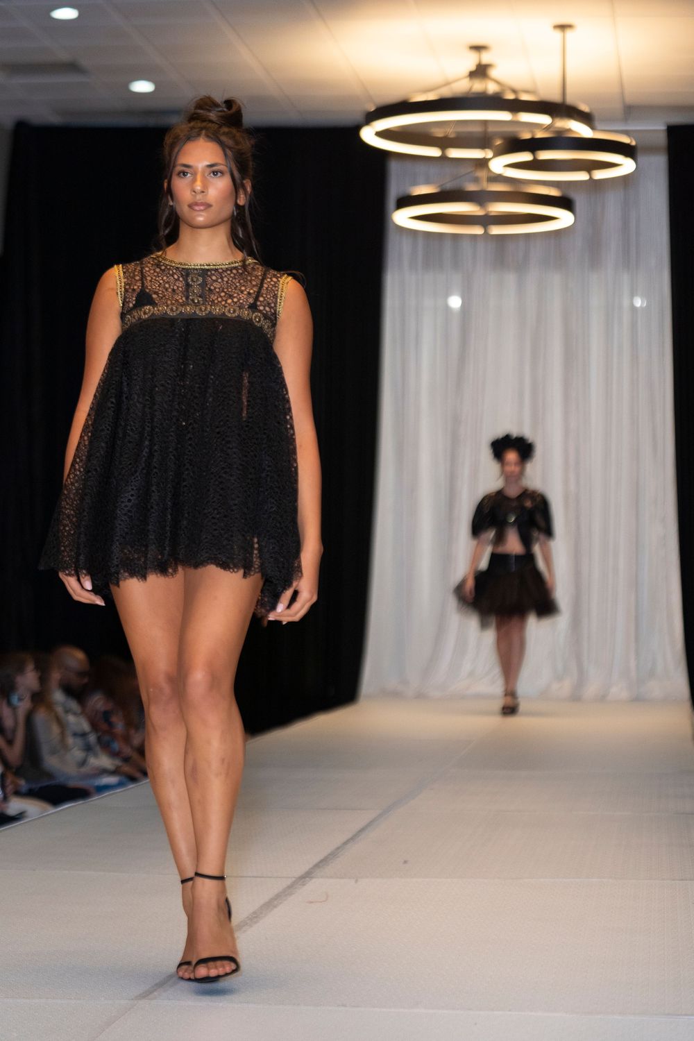 Little black dress with lace detail and flowing silhouette showcased on catwalk.