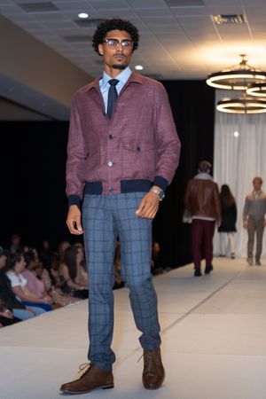 Model showcases burgundy blazer with plaid pants and brown boots on fashion runway catwalk.