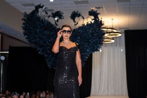 A performer in a sparkly black dress and blue feathered headpiece performs on stage during a cabaret show.