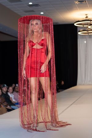Fashion model wearing red lingerie with dramatic floor-length red beaded fringe curtain on runway.