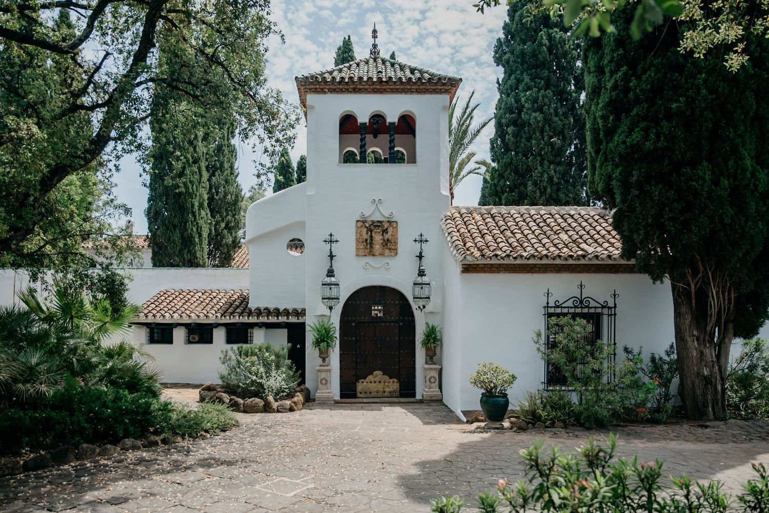 Spanish-style white church building with terracotta roof and cypress trees.