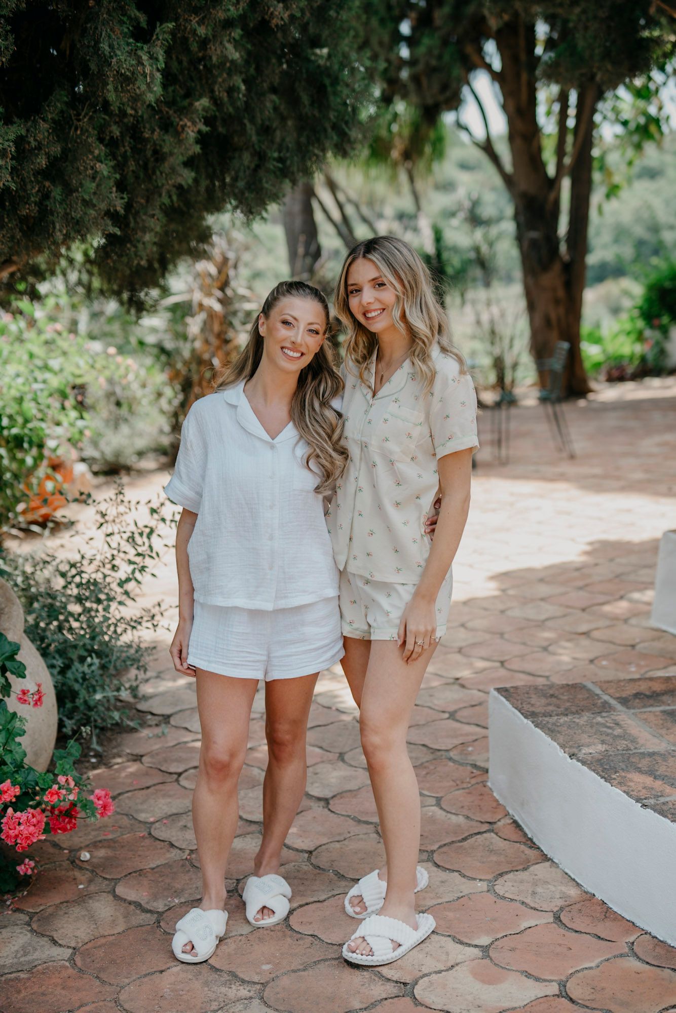Wedding party members in matching white pajama sets pose on stone patio.