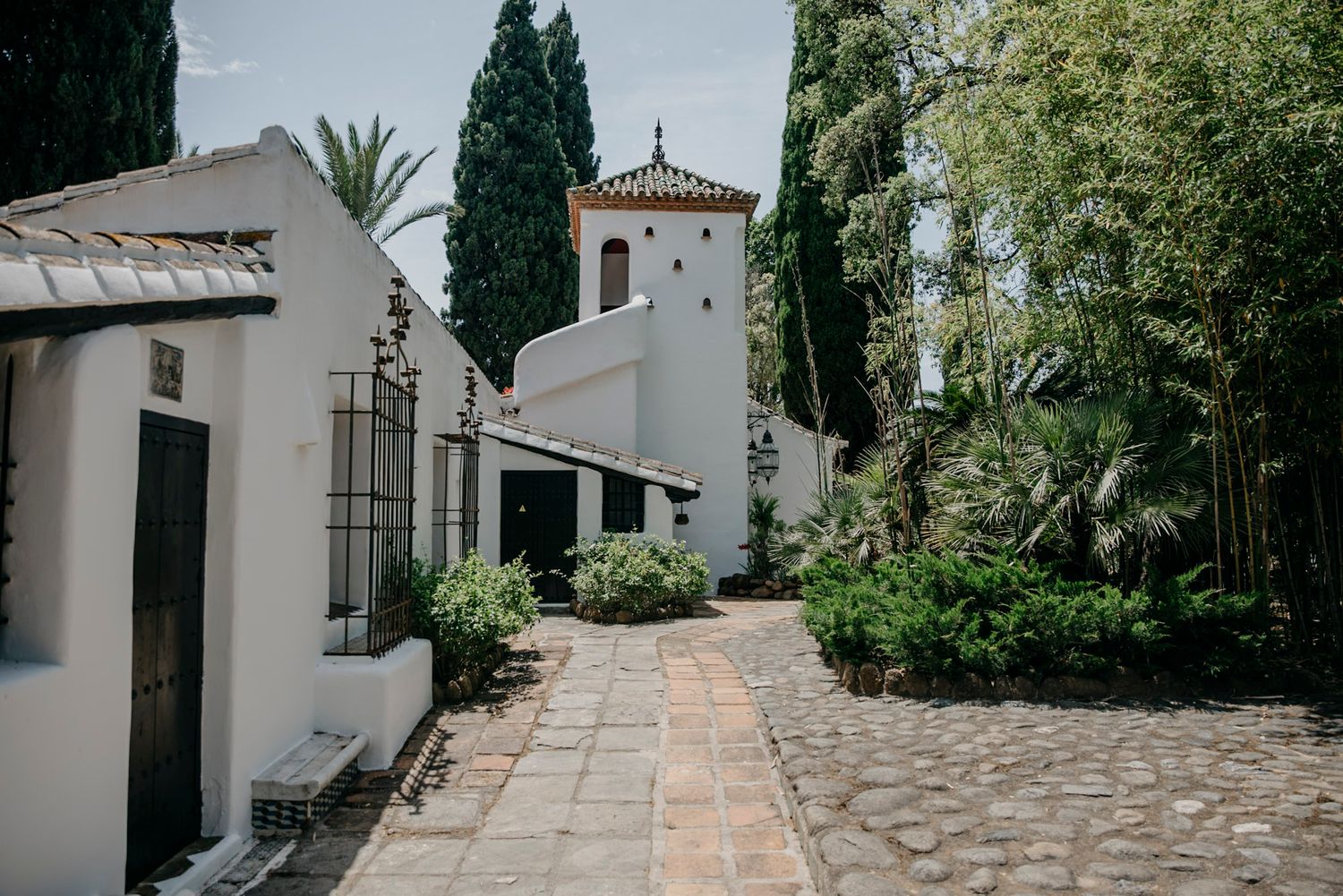 Stone pathway leading through Mediterranean garden with cypress trees and white buildings.