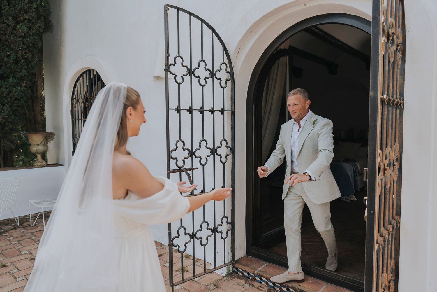 Elegant wrought iron gate entrance with white stucco walls and lush greenery in background.