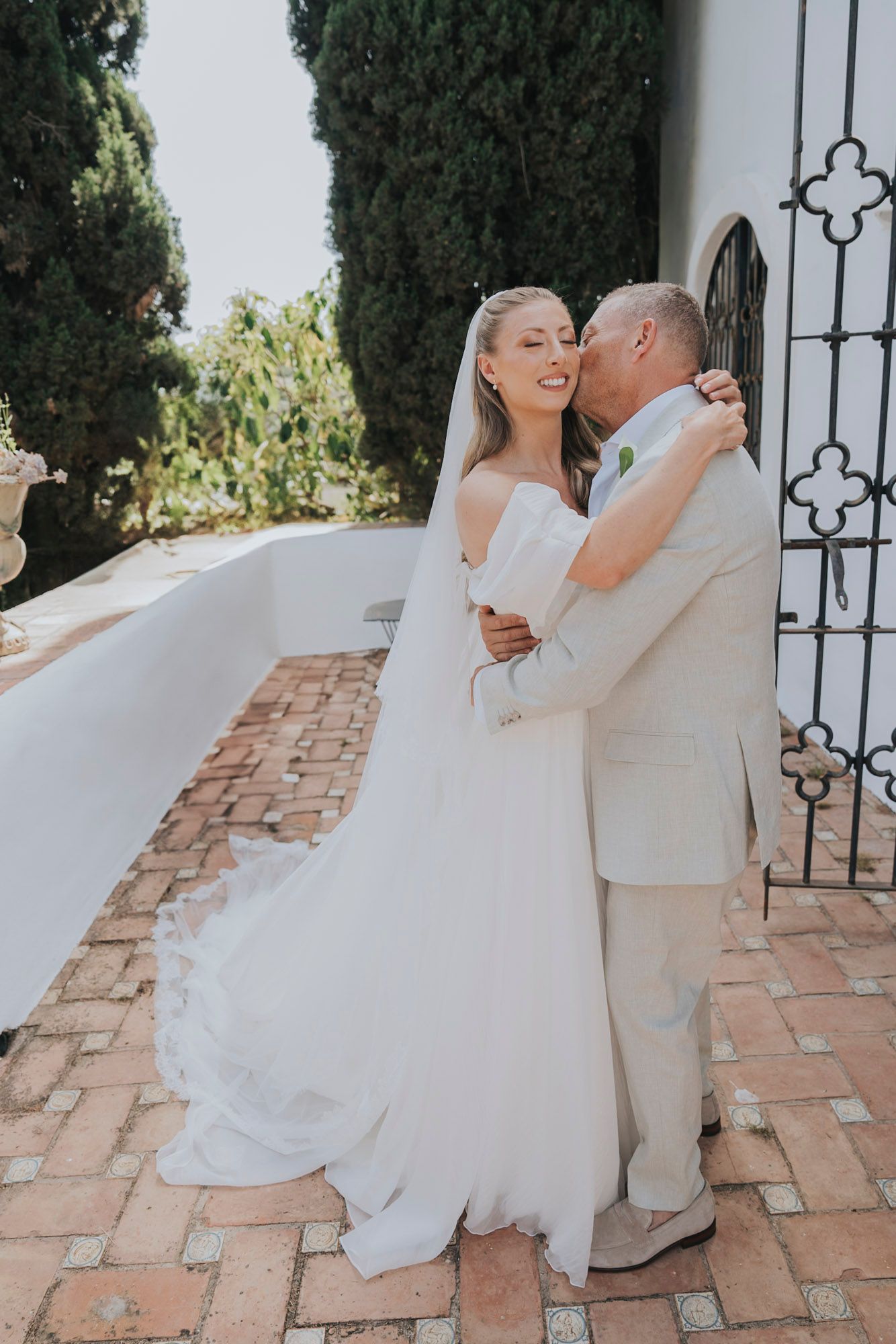 Romantic wedding couple dancing on terracotta tiles surrounded by cypress trees.