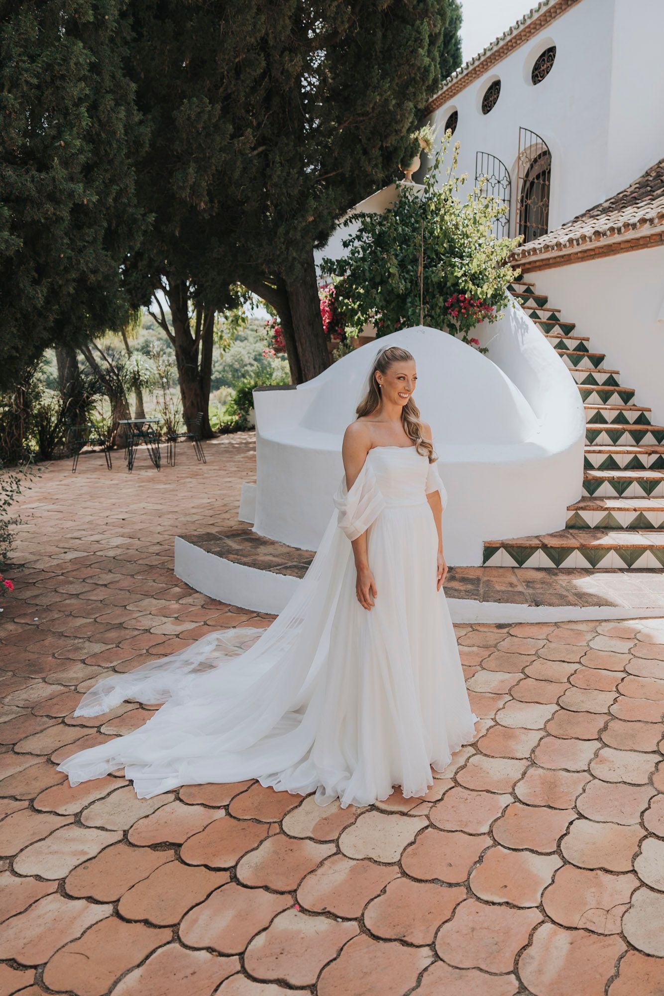 Flowing white wedding dress captured in motion on terracotta tiles against white villa backdrop.