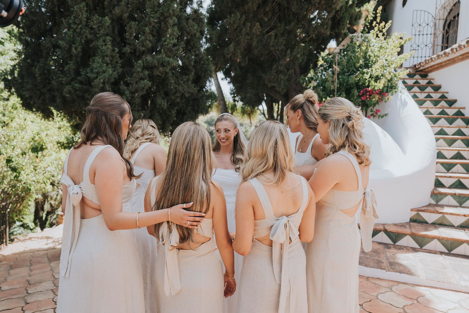 Wedding party in soft neutral dresses walking along Mediterranean villa pathway.