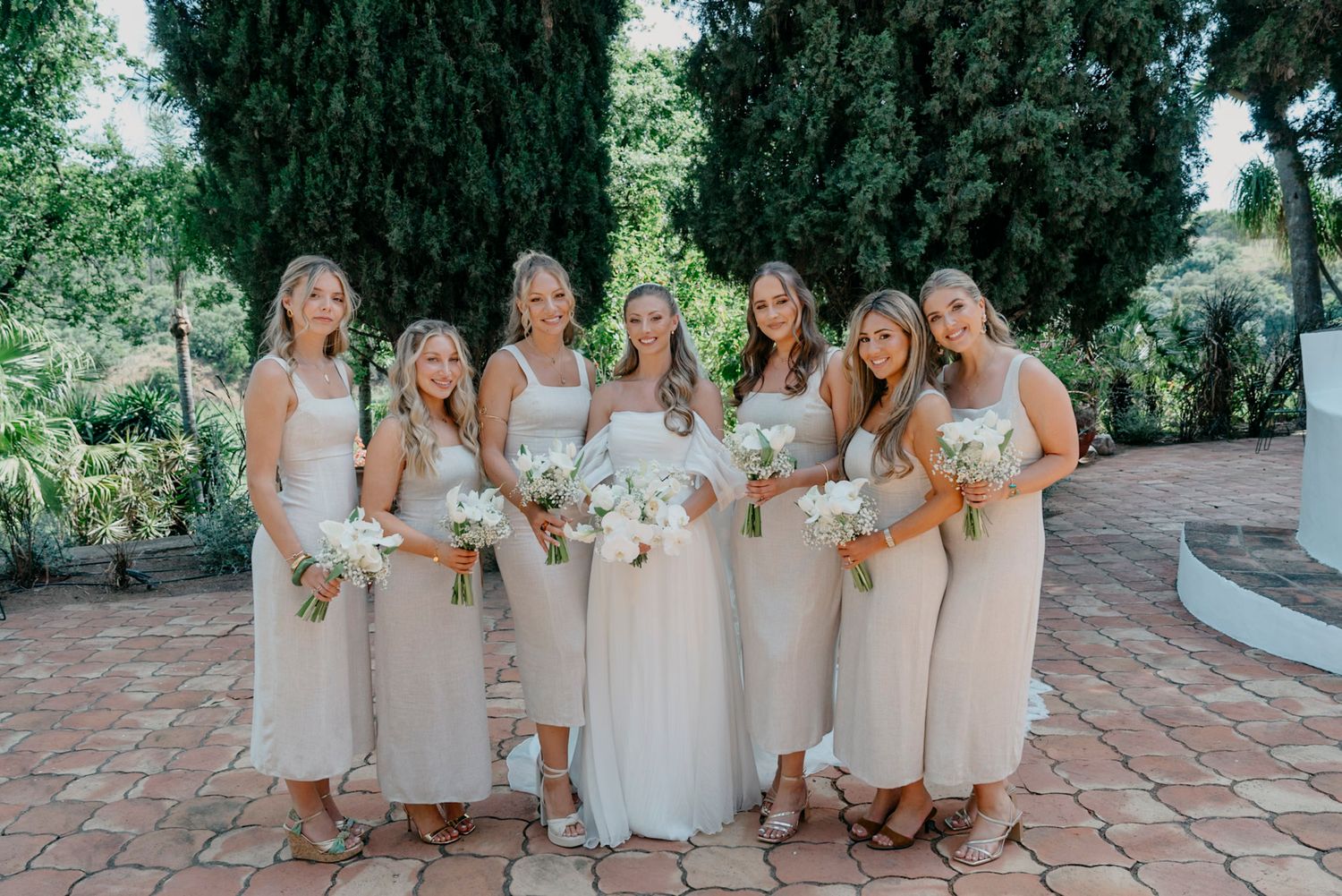 Bridesmaids in neutral dresses gather for photos at Spanish-style wedding venue.