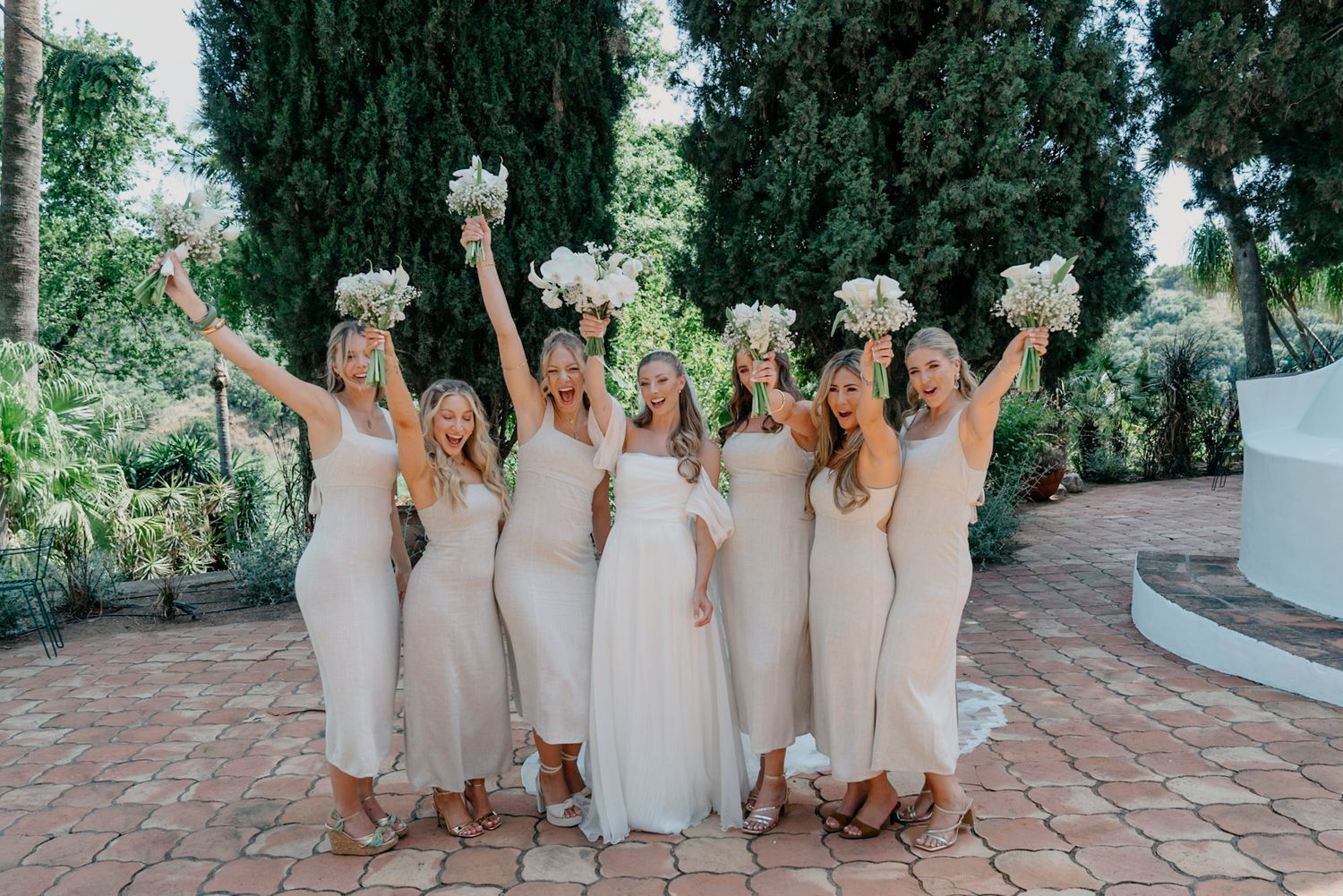 Bridesmaids in cream-colored dresses posing together on stone steps.