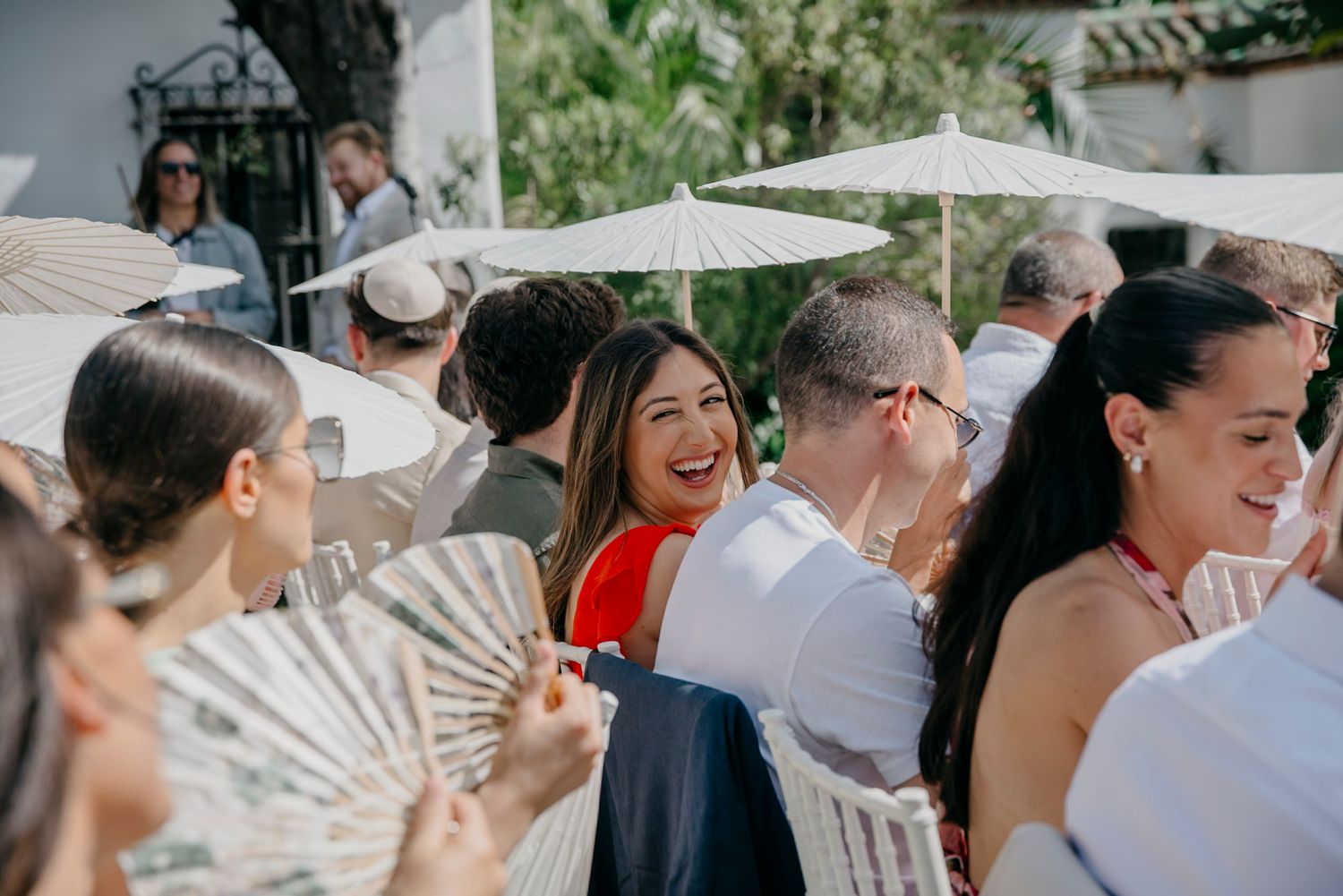 Wedding guests mingle and socialize under outdoor umbrellas at a garden reception.