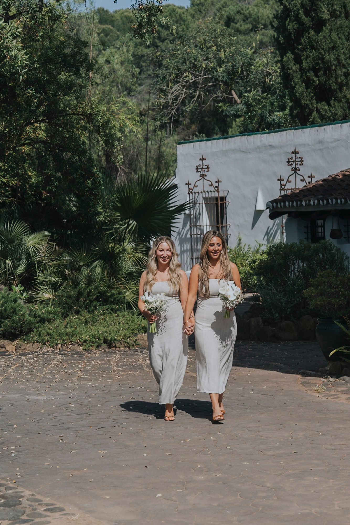 Bridesmaids in white dresses walking together on stone pathway at outdoor venue.