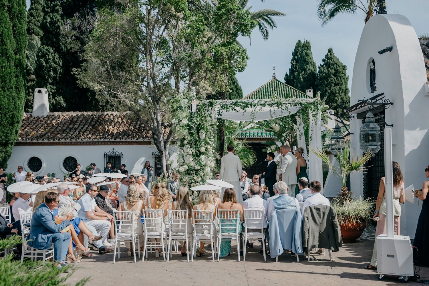 Elegant outdoor wedding reception setup with white chairs and tropical landscaping.