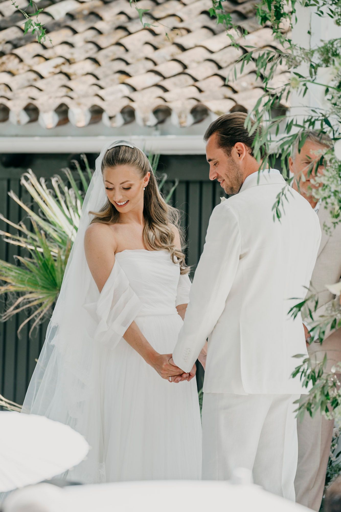 Elegant wedding ceremony setup with white decor and flowing fabrics against a Spanish-style building.