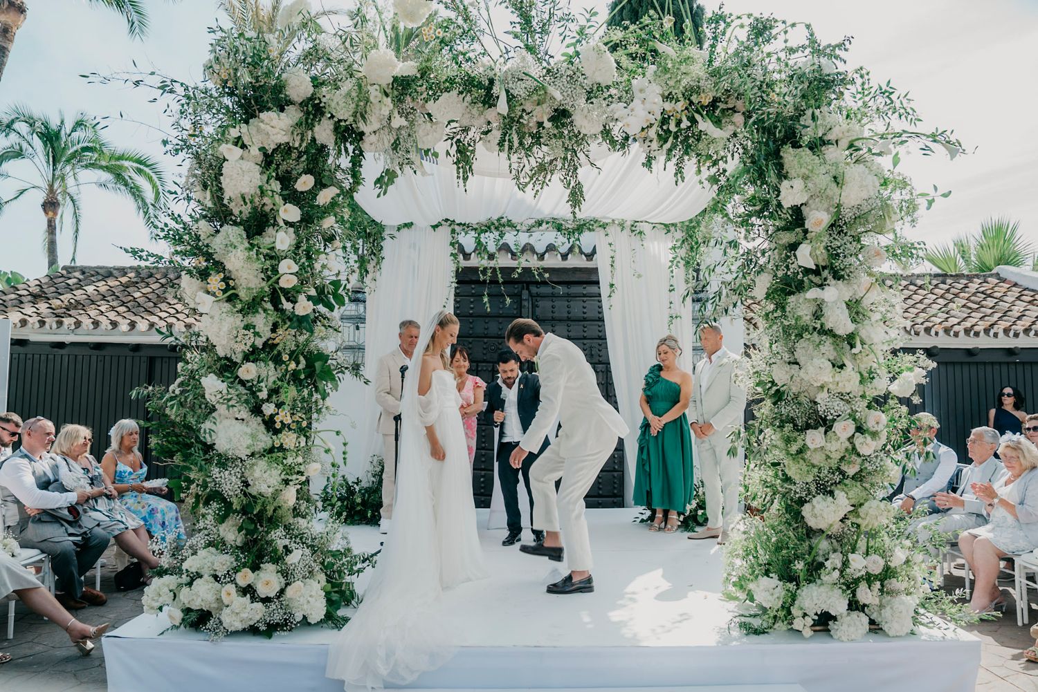 Luxurious outdoor wedding ceremony space decorated with white floral arrangements and hanging greenery.