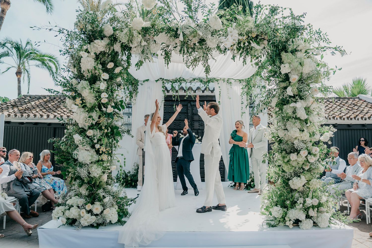 Wedding ceremony venue with white floral arrangements and guests seated in white chairs.