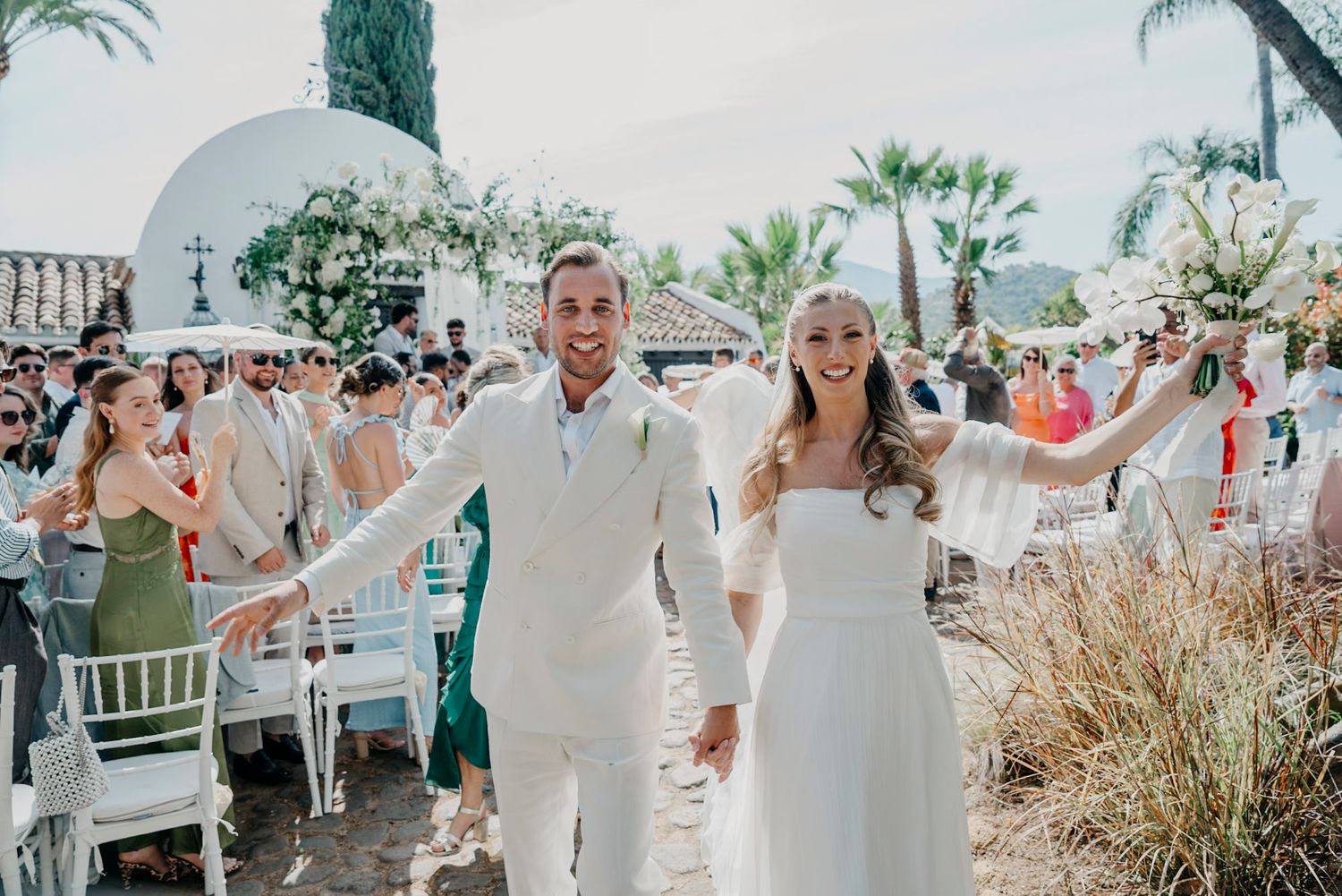 Wedding celebration at an elegant outdoor venue with palm trees and white decor.
