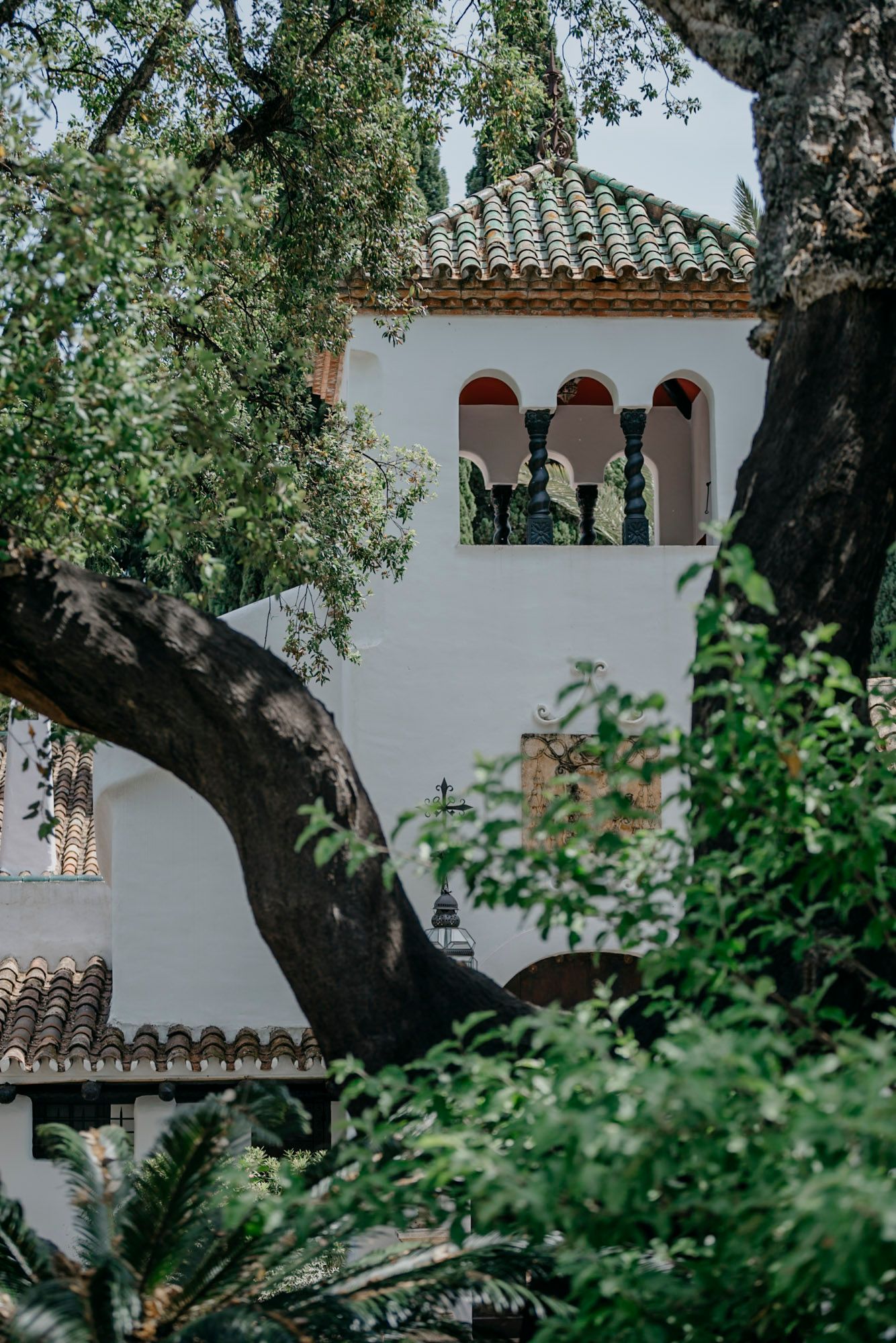 White stucco building with Spanish-style terracotta roof tiles and arched windows framed by lush green foliage.