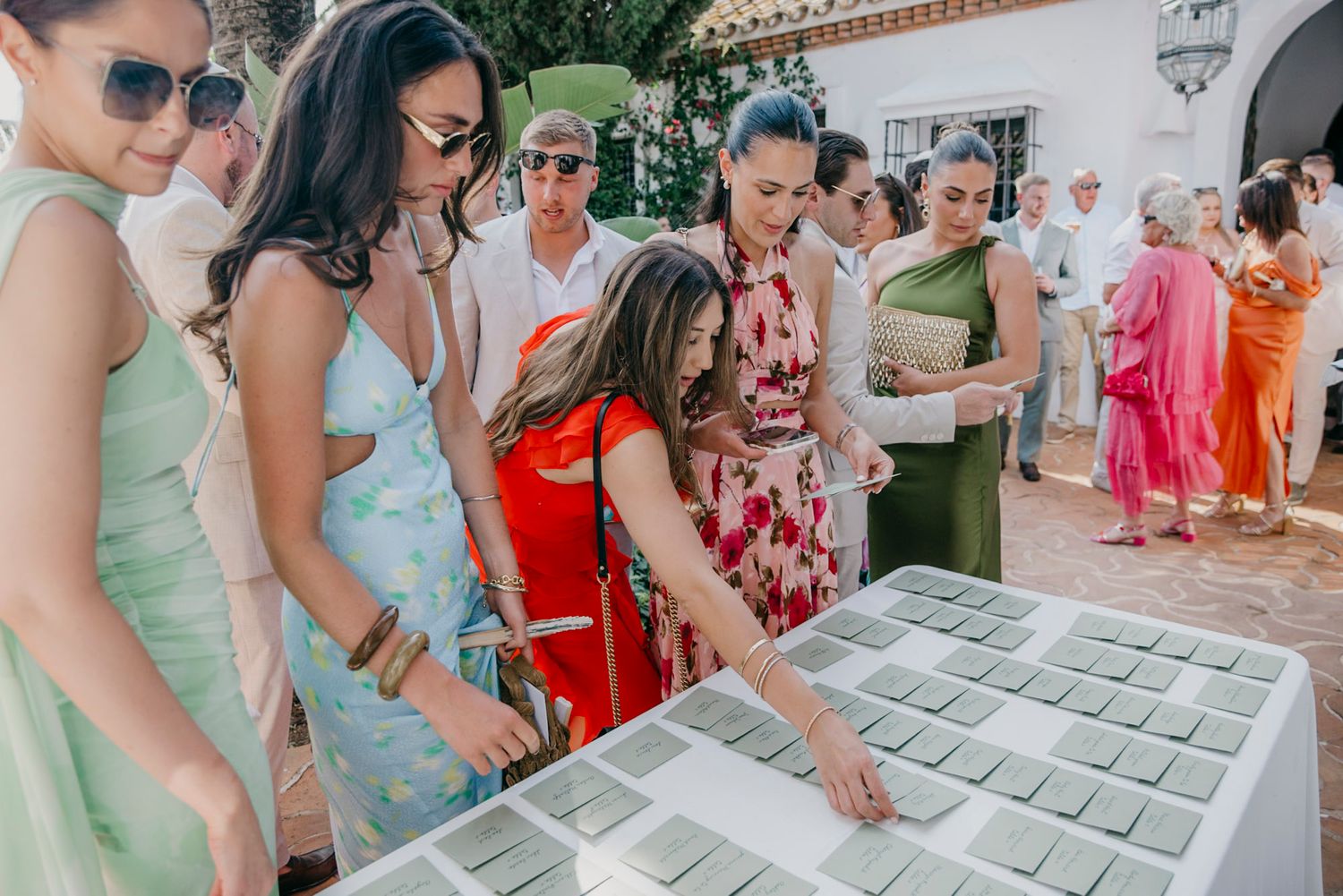Wedding guests interacting with seating chart display at outdoor reception venue.