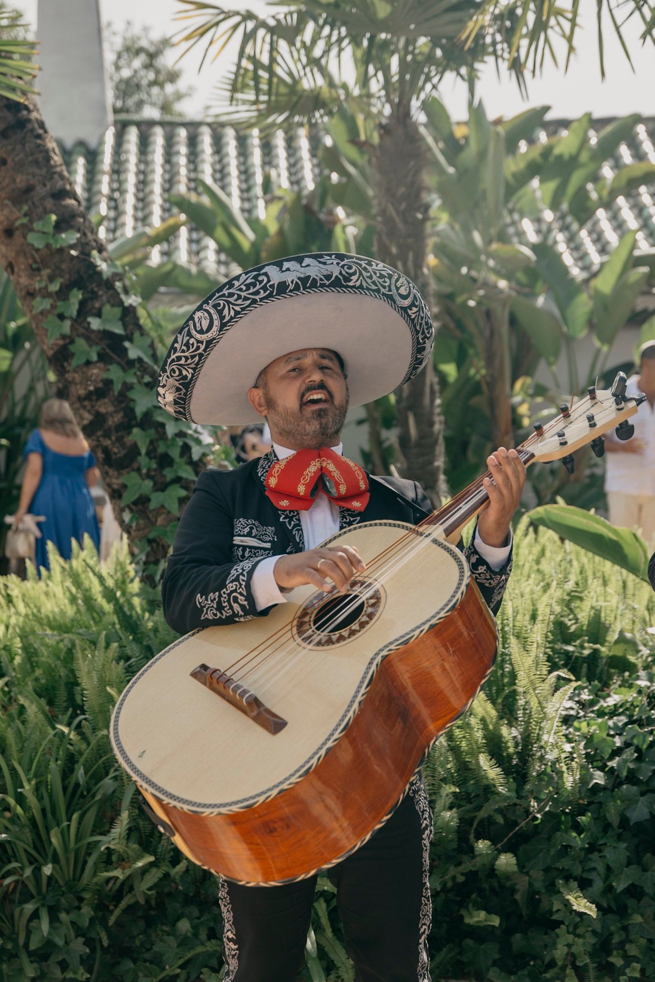 Mariachi musician passionately playing a traditional guitarrón against a lush tropical garden backdrop.