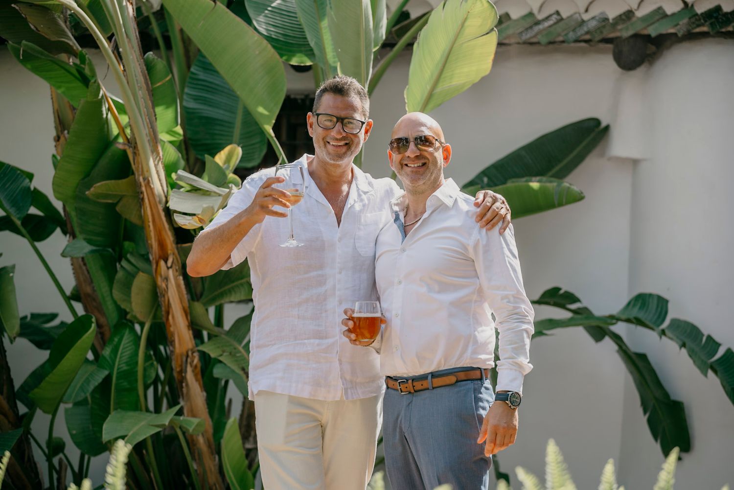 Wedding party members in all-white attire pose in tropical garden setting.