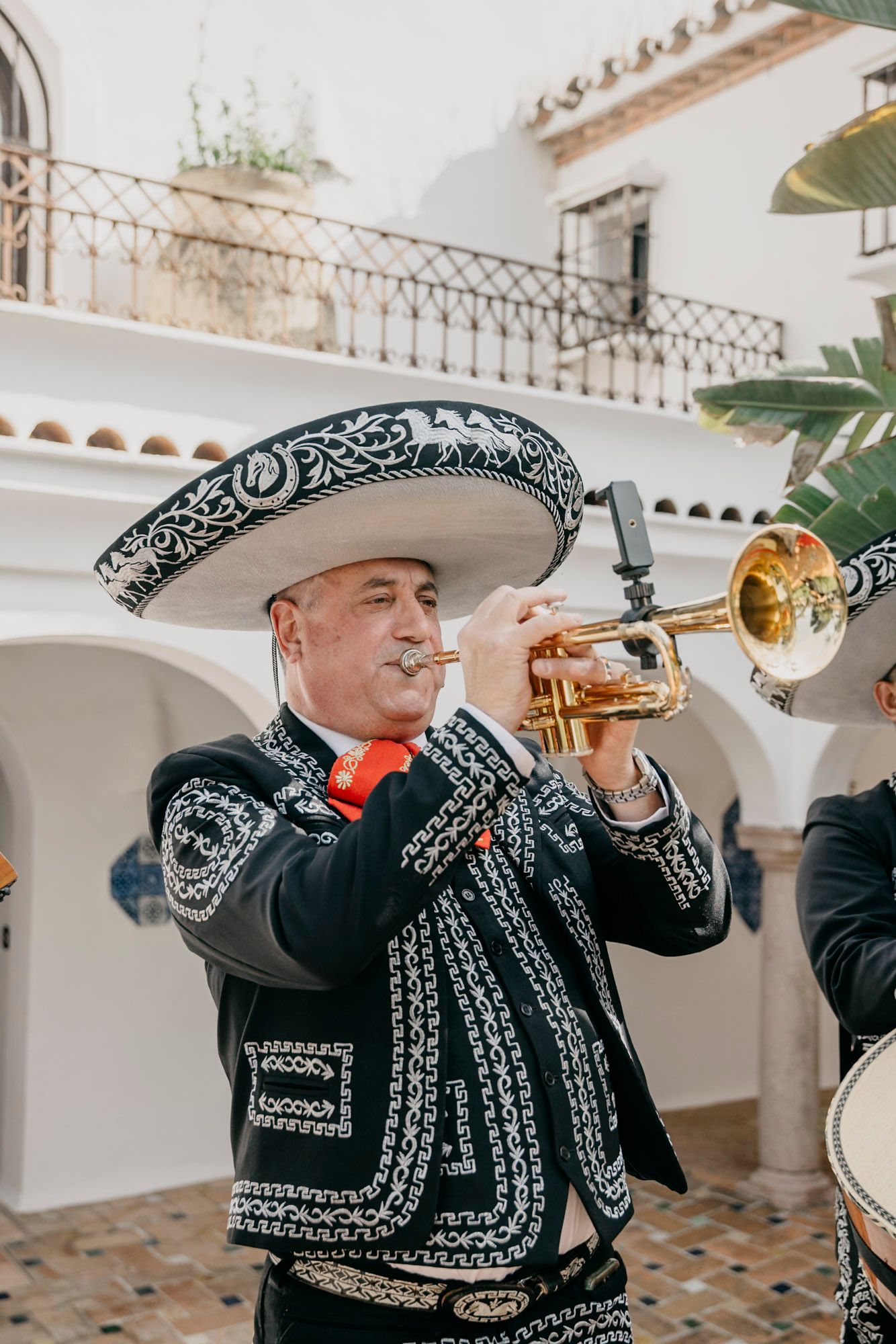 Mariachi band members in traditional black and silver embroidered suits playing trumpets at an event.