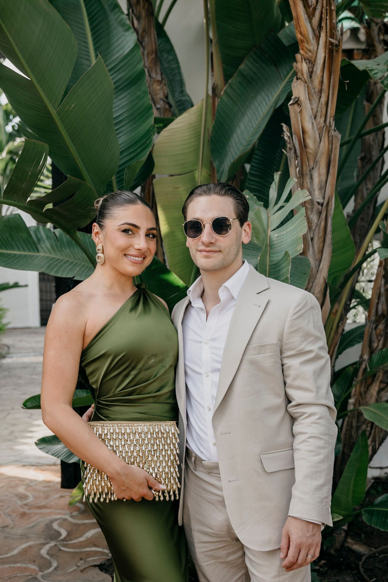 Couple posing together against tropical foliage backdrop.