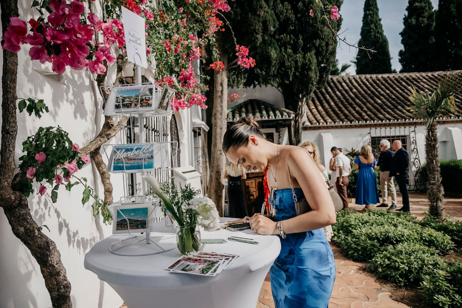Guest signing guestbook at outdoor Mediterranean wedding venue with bougainvillea flowers.