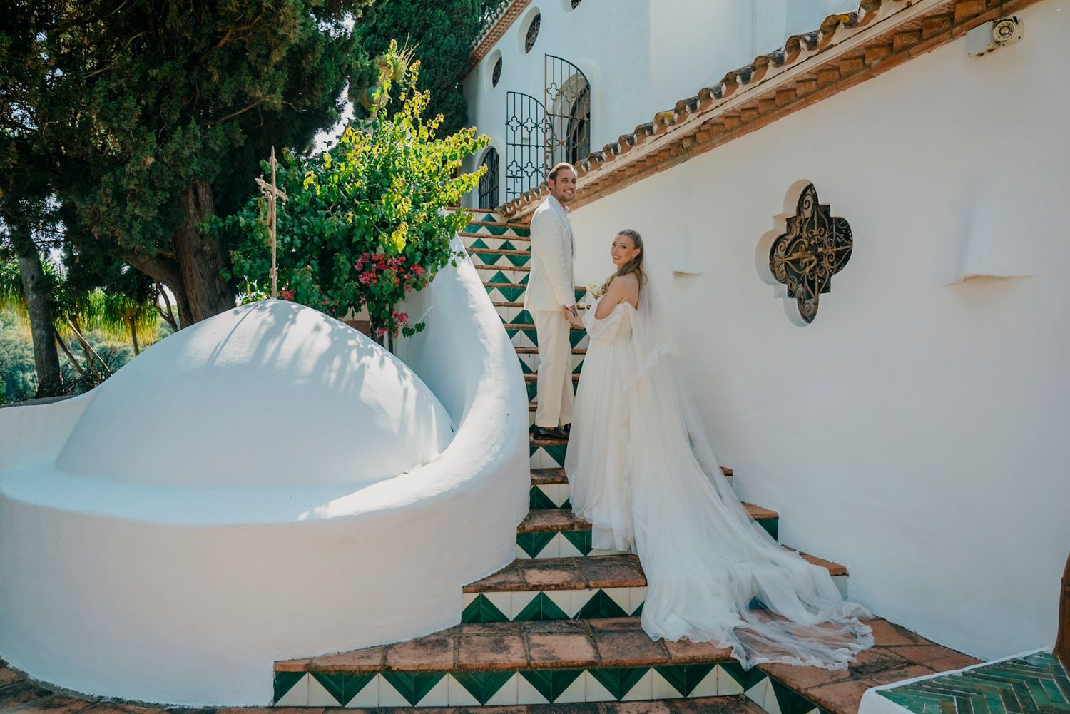 Elegant white wedding dress trailing along Mediterranean-style architecture with white walls and archways.