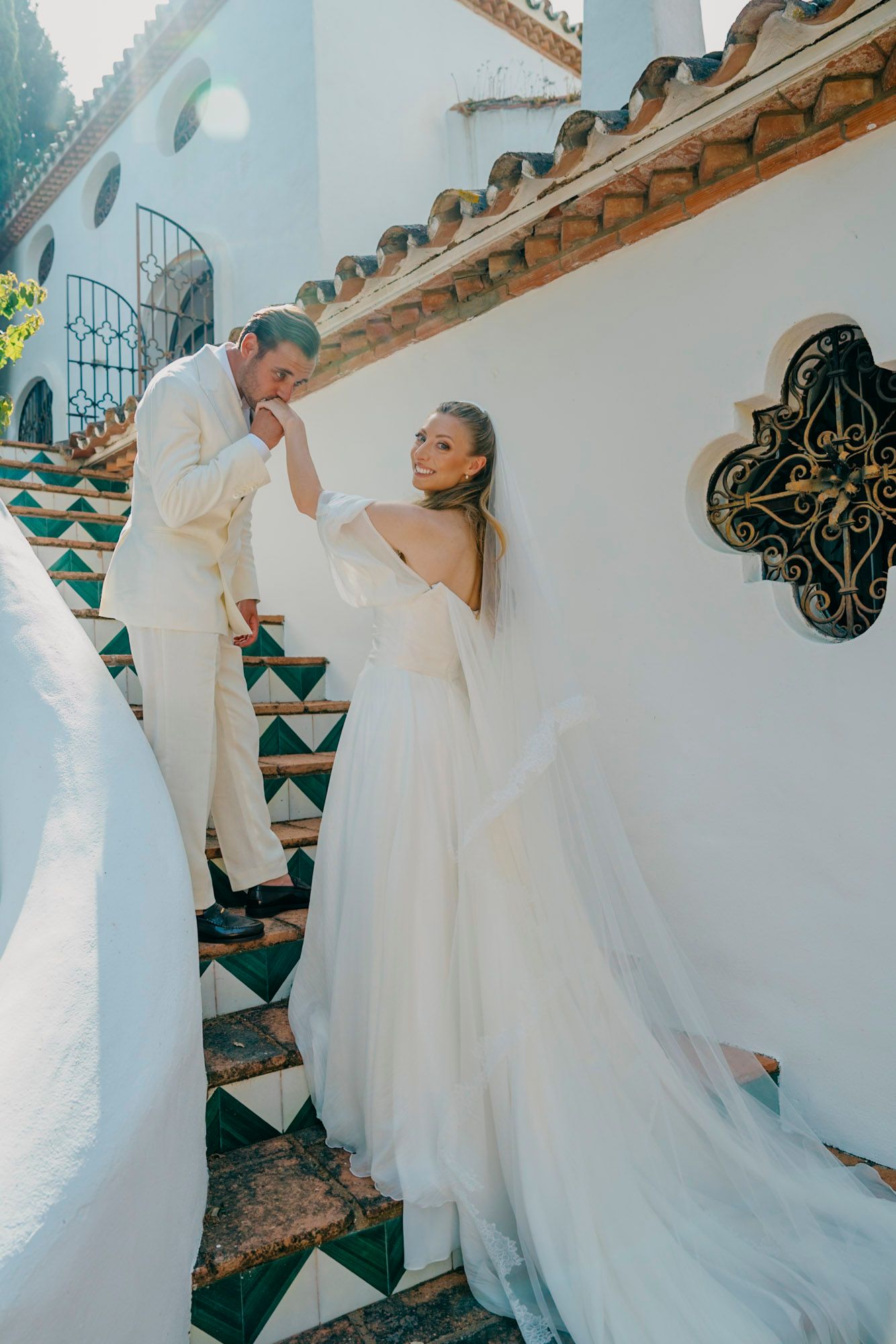 Couple posing on decorative tiled steps of white Mediterranean villa.