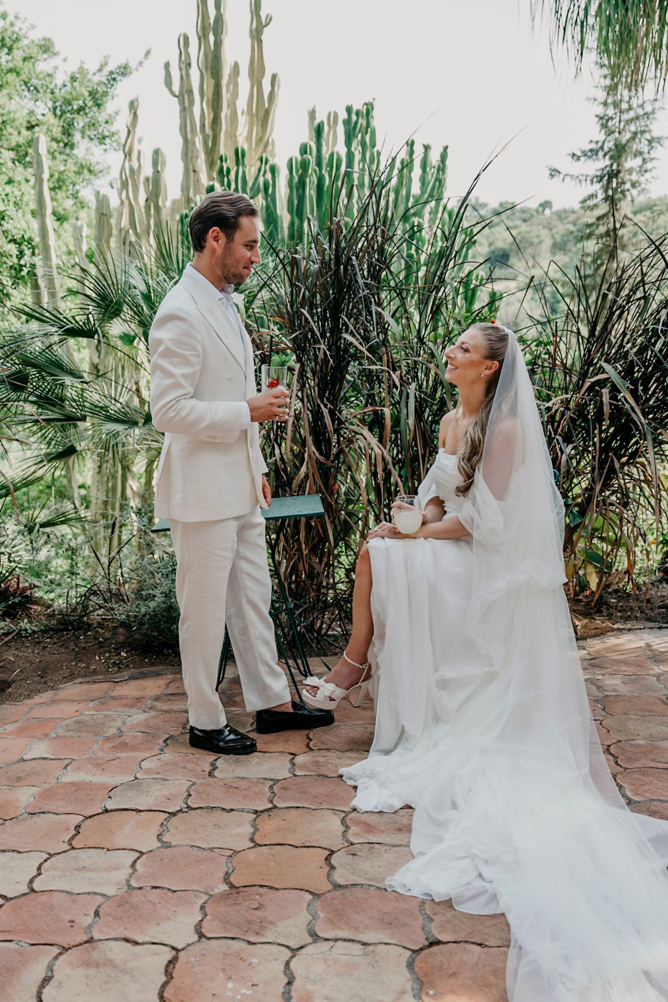Couple sharing a romantic first look moment in white attire on a stone patio surrounded by cacti.