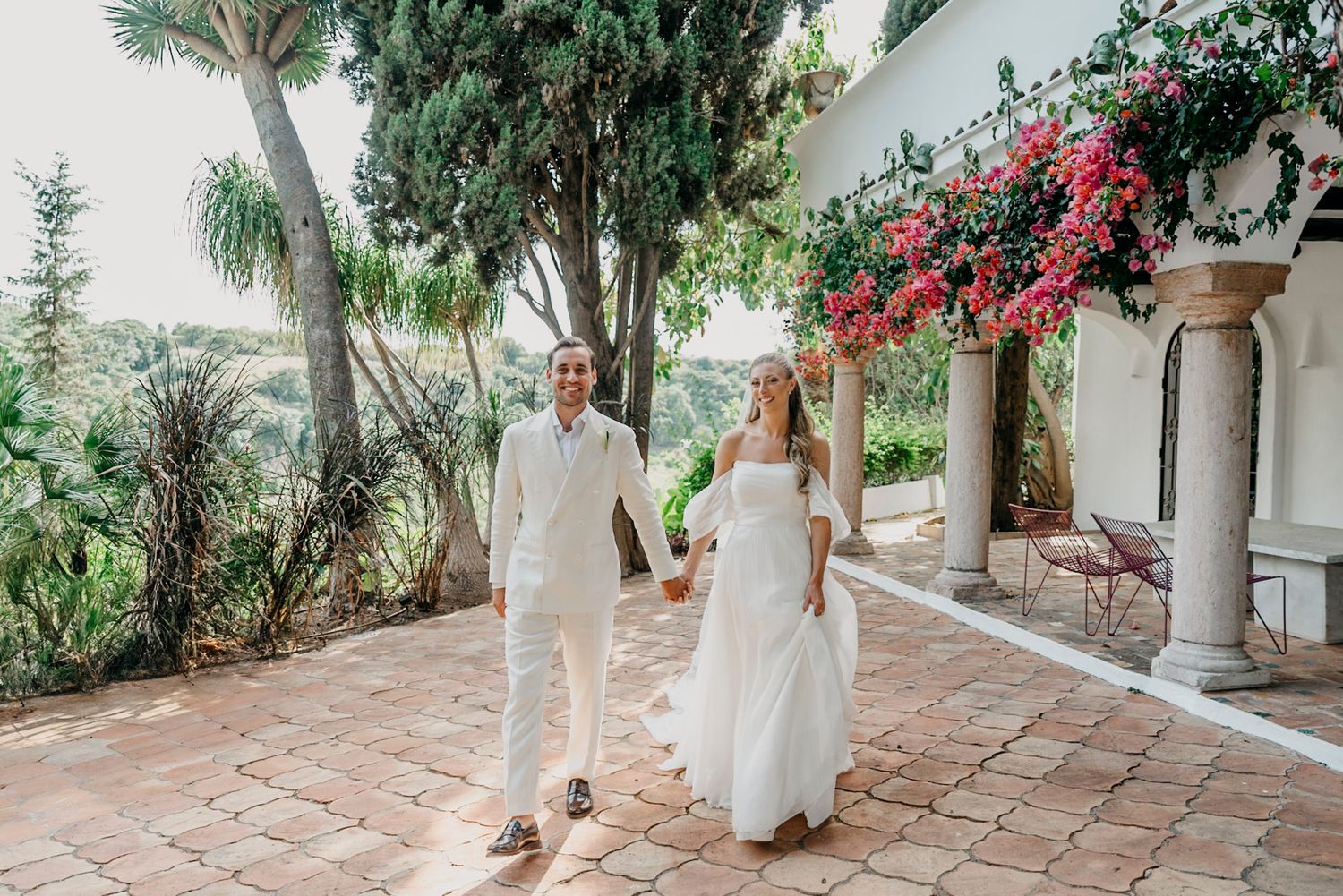 Elegant stone walkway lined with tropical plants and red bougainvillea flowers at a Spanish-style venue.
