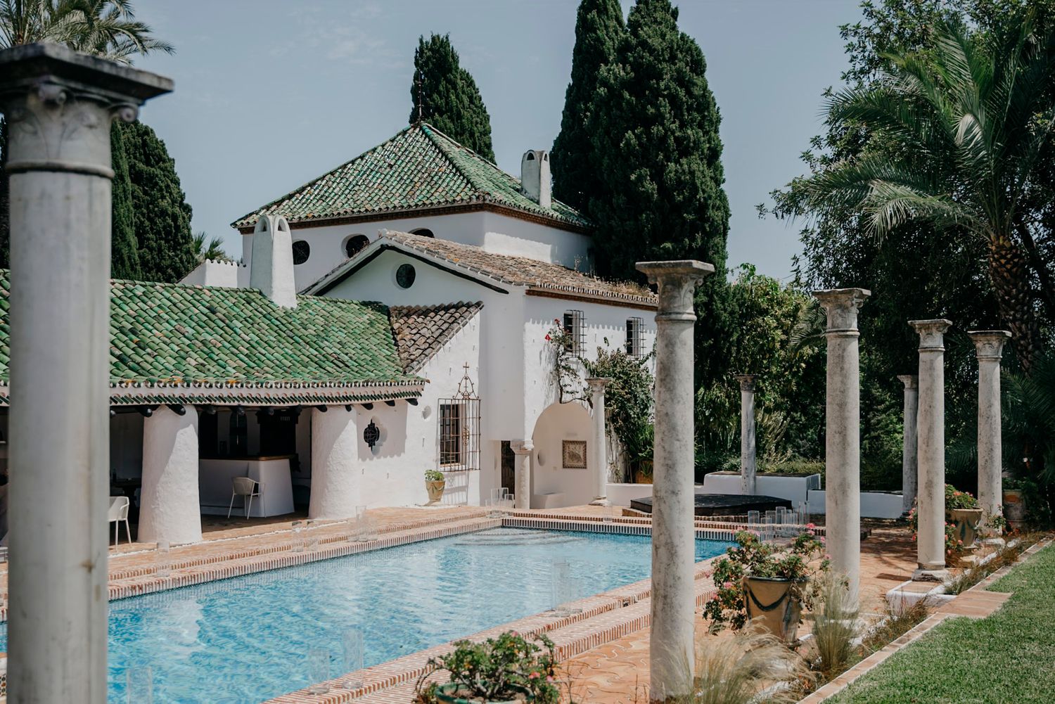 Mediterranean villa courtyard featuring white columns and a serene swimming pool surrounded by cypress trees.